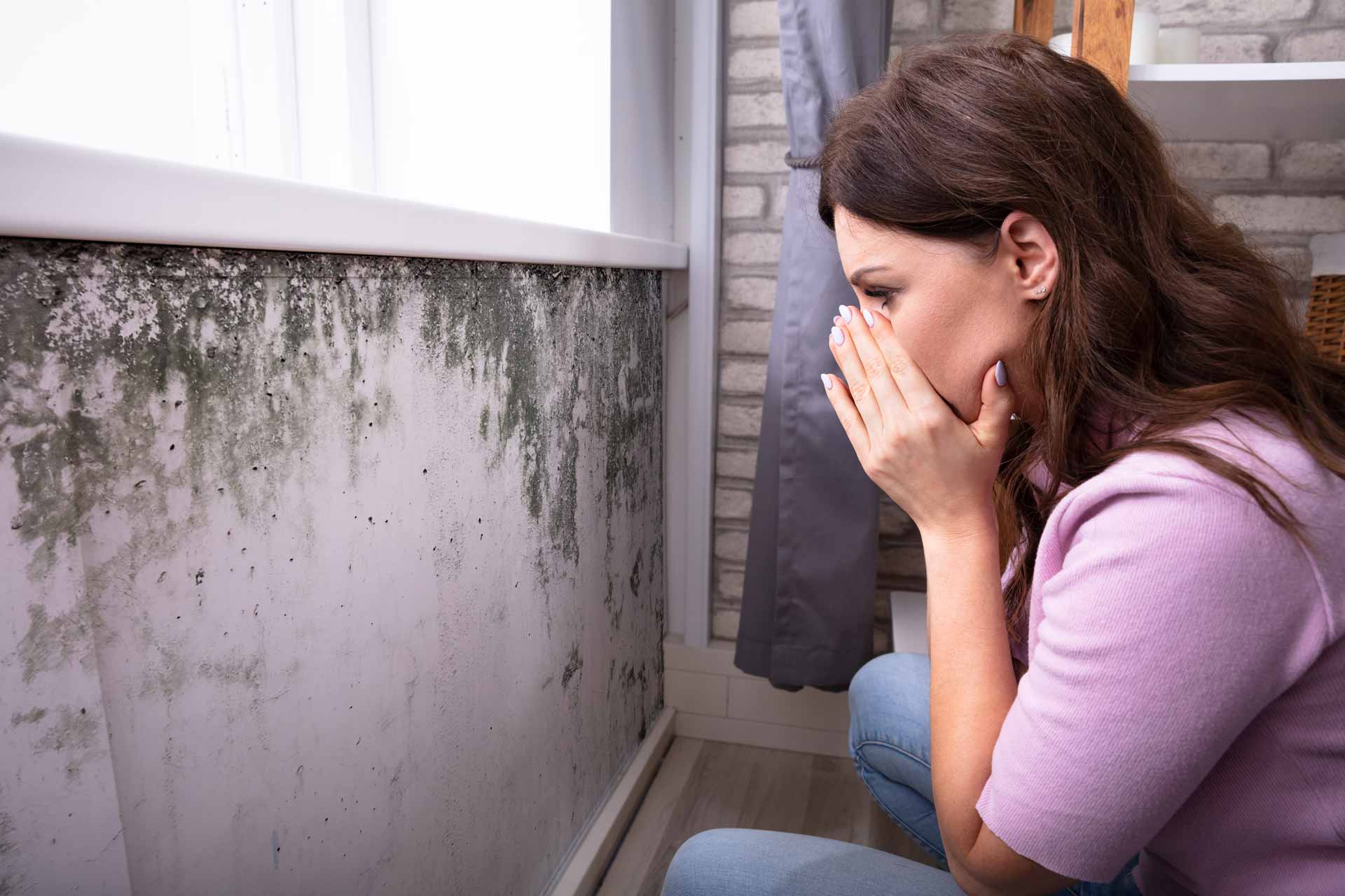 Woman looking at moldy wall in home with shocked expression